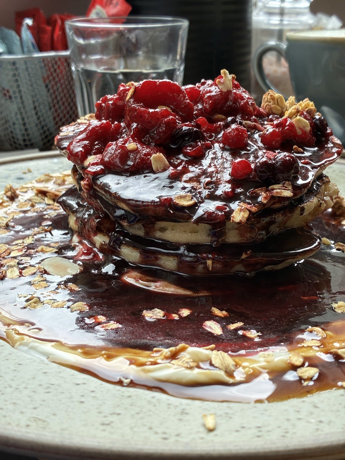 A tall stack of pancakes under a glossy berry compote with raspberries, blueberries and toasted oats.